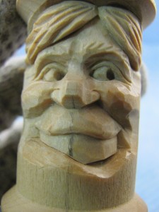 Draw the upper edge of the lower lip and cut above it with the V-tool. Once again trace the cut and begin removing wood to shape the teeth. Keep in mind the teeth should appear to protrude from behind the upper lip and tuck behind the lower lip. The curve of the teeth should be the same on both sides of the center line. Invert the spool to double check the balance. Because the lower lip dips below the upper teeth on the right side, mark a line for the lower edge of the teeth. I use a knife to create the negative space between the teeth and the lower lip. Rest the blade on the lip as a guide. This will make the lip disappear into the mouth. A variation of this face could show a lower tooth (or two) instead of the opening.