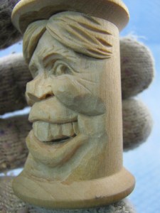 Shape the corners of the mouth and lip with the 10mm #11 gouge. The lower lip tapers as it approaches the corners, both from both the bottom and the side. Notice the vertical opening that connects the upper and lower lips. Leave a little mound of wood on the cheek side of the vertical cut. Continue smoothing the area under the lip toward the sides of the spool. Also notice I used a 2mm #9 gouge to create nostril openings.